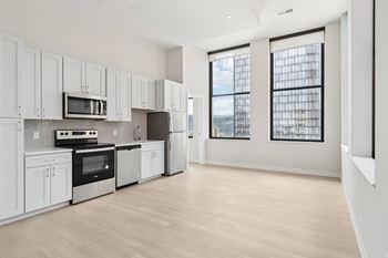 A kitchen with white cabinets and appliances, a wooden floor, and a view of the city through the windows.
